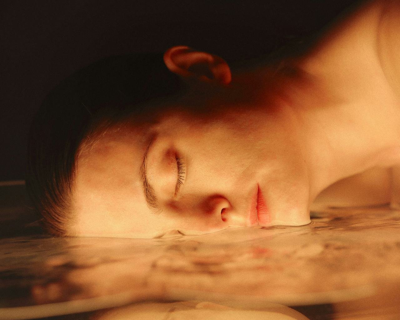 Woman with eyes closed, glowing skin resting in warm water